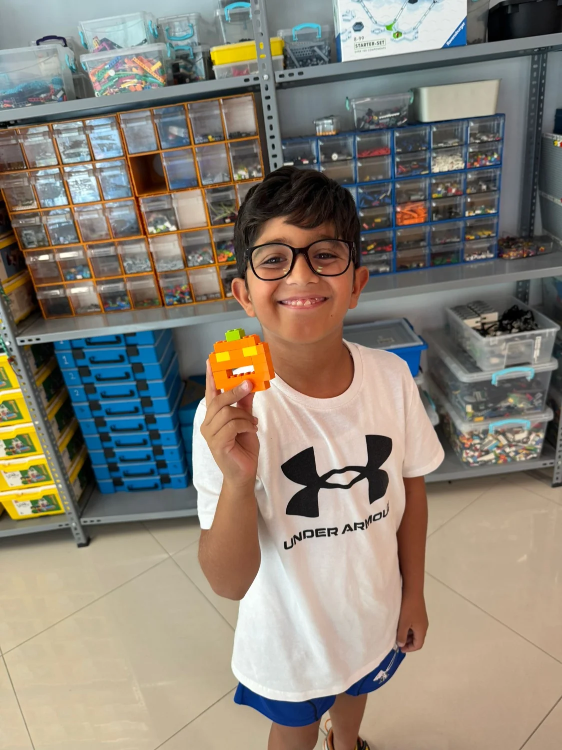 A smiling child showing an orange model made from building bricks